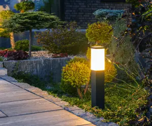 Two bollard lights placed along a garden path at night. Custom landscape lighting by Grasshoppers is an excellent way to brighten up your property.