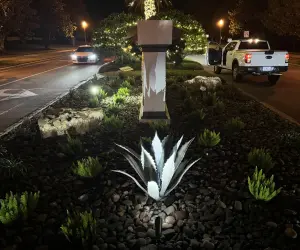 A closeup of an LED light shining on a plant and neighborhood sign. Contact Grasshoppers today to install outdoor LED lights for your home or business.